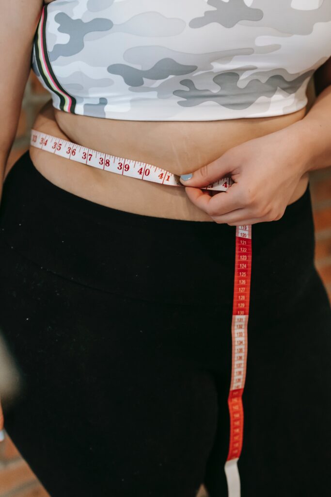 Woman wrapping a measuring tape around her waist to track her weight loss progress.
